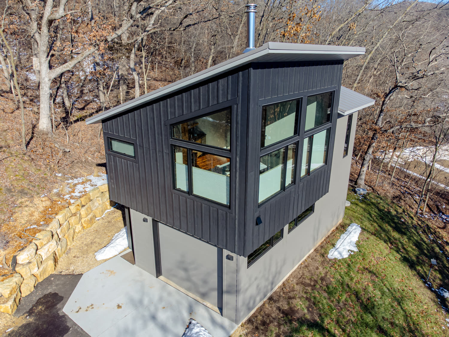 Compact detached dwelling with dark vertical siding and corner windows, built over a garage