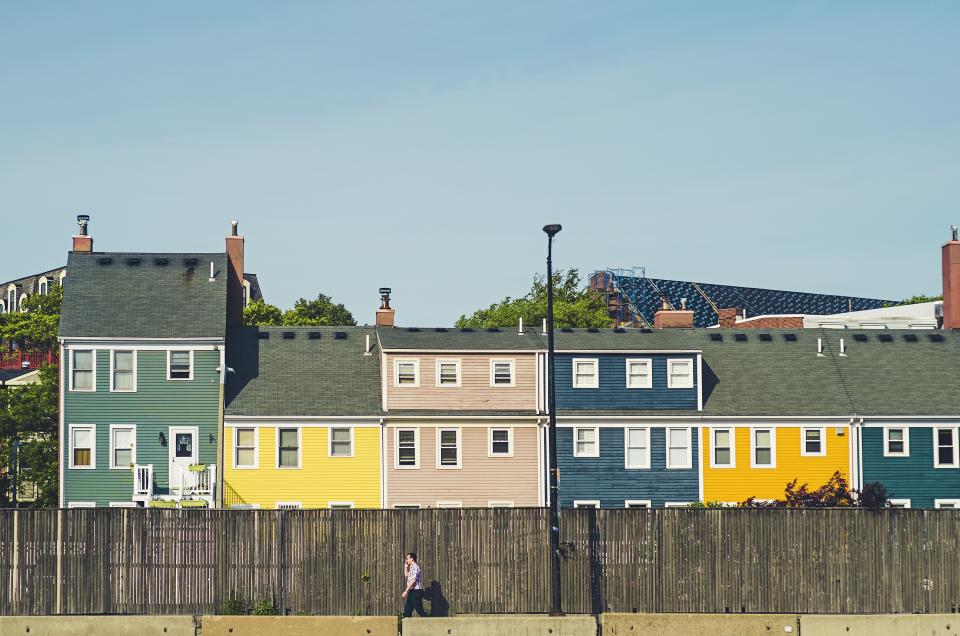 Row of small attached homes painted green, yellow and blue behind a timber fence