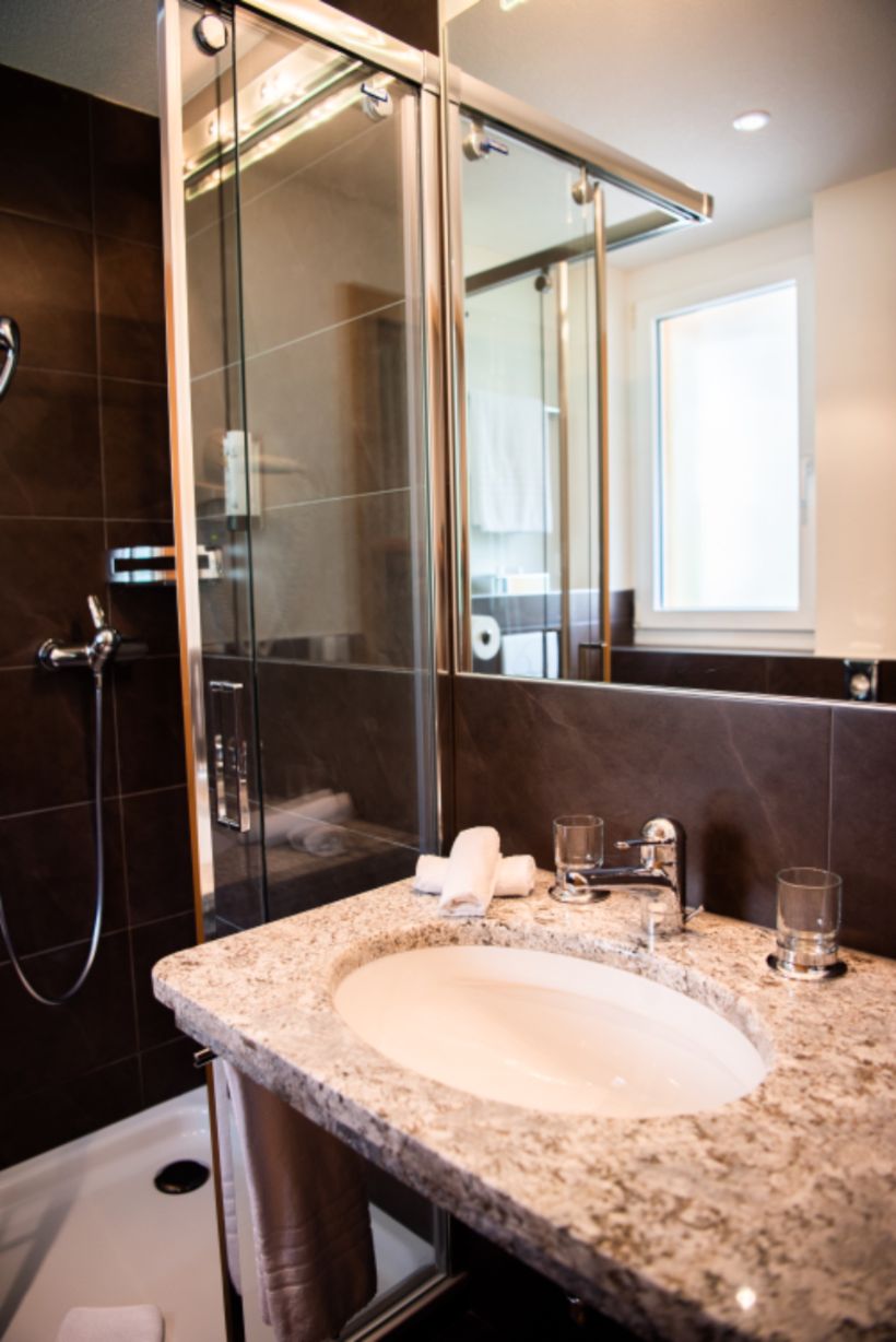 Bathroom vanity with a stone top beside a glass shower