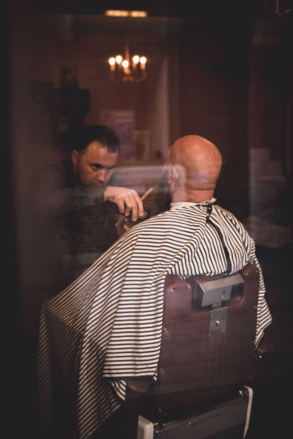 Barber cutting a client&rsquo;s hair in a warmly lit shop
